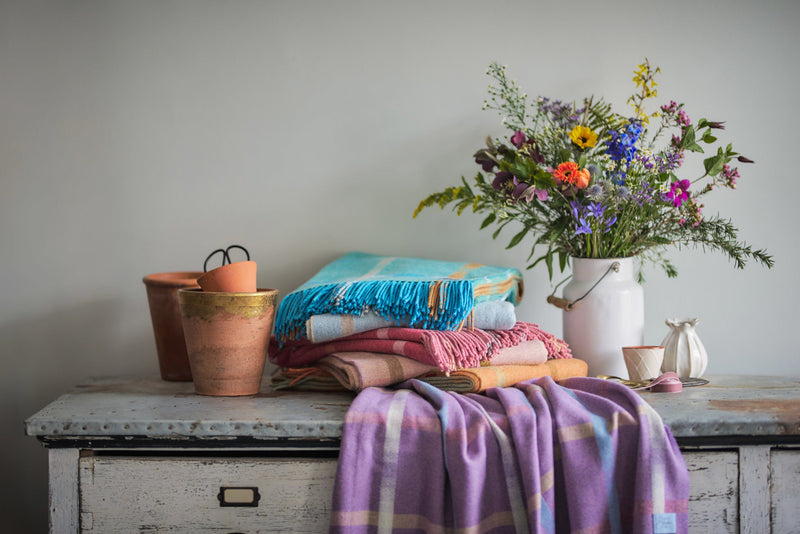 Garden Flowers Forget-Me-Not Merino Lambswool Blanket drapes over a rustic dresser, styled with plant pots, a wildflower vase, and cozy home décor.