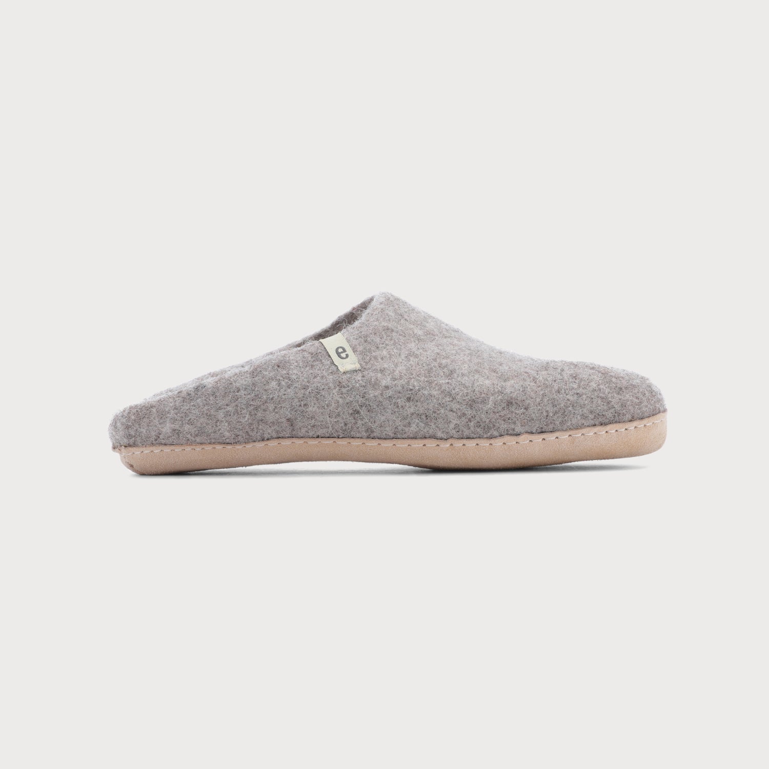 Wool Felt Slippers: Natural grey slipper with white sole, featuring a soft suede bottom and white tag, handcrafted in Nepal for indoor use.