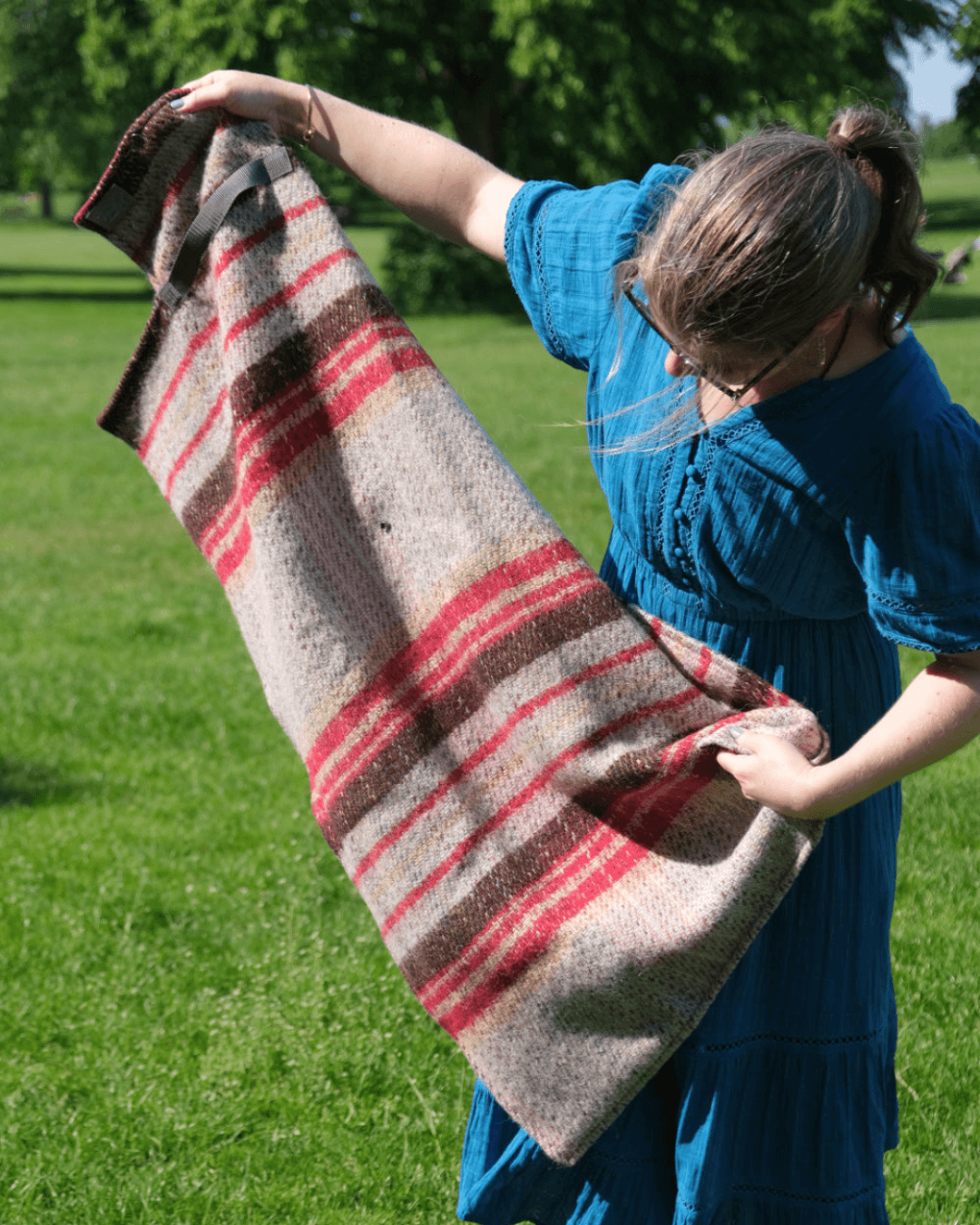 Person holding out the Individual picnic blanket in the park