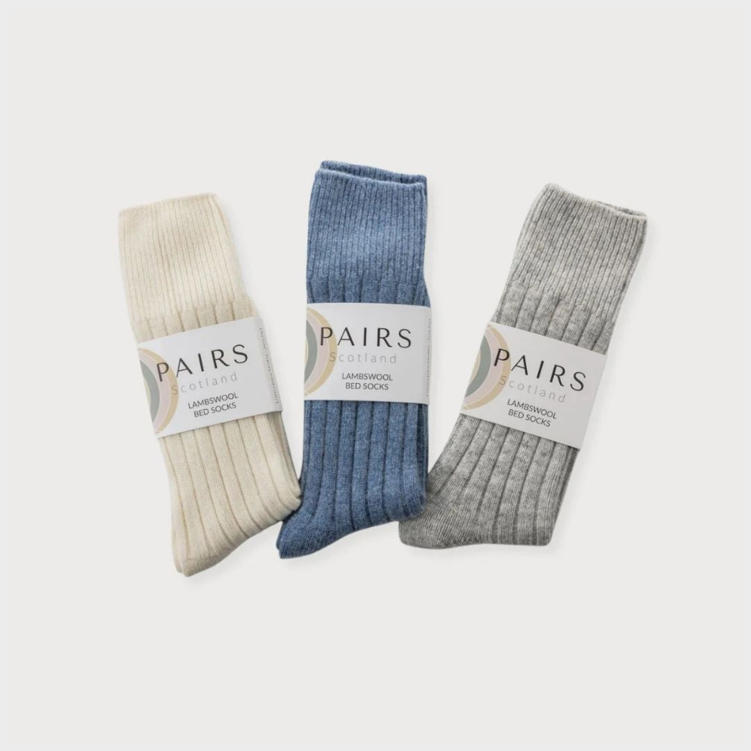 Bright Friday Blanket Bundle: Curious, featuring three folded lambswool bed socks from PAIRS Scotland, labeled by color: off-white, denim blue, light gray.