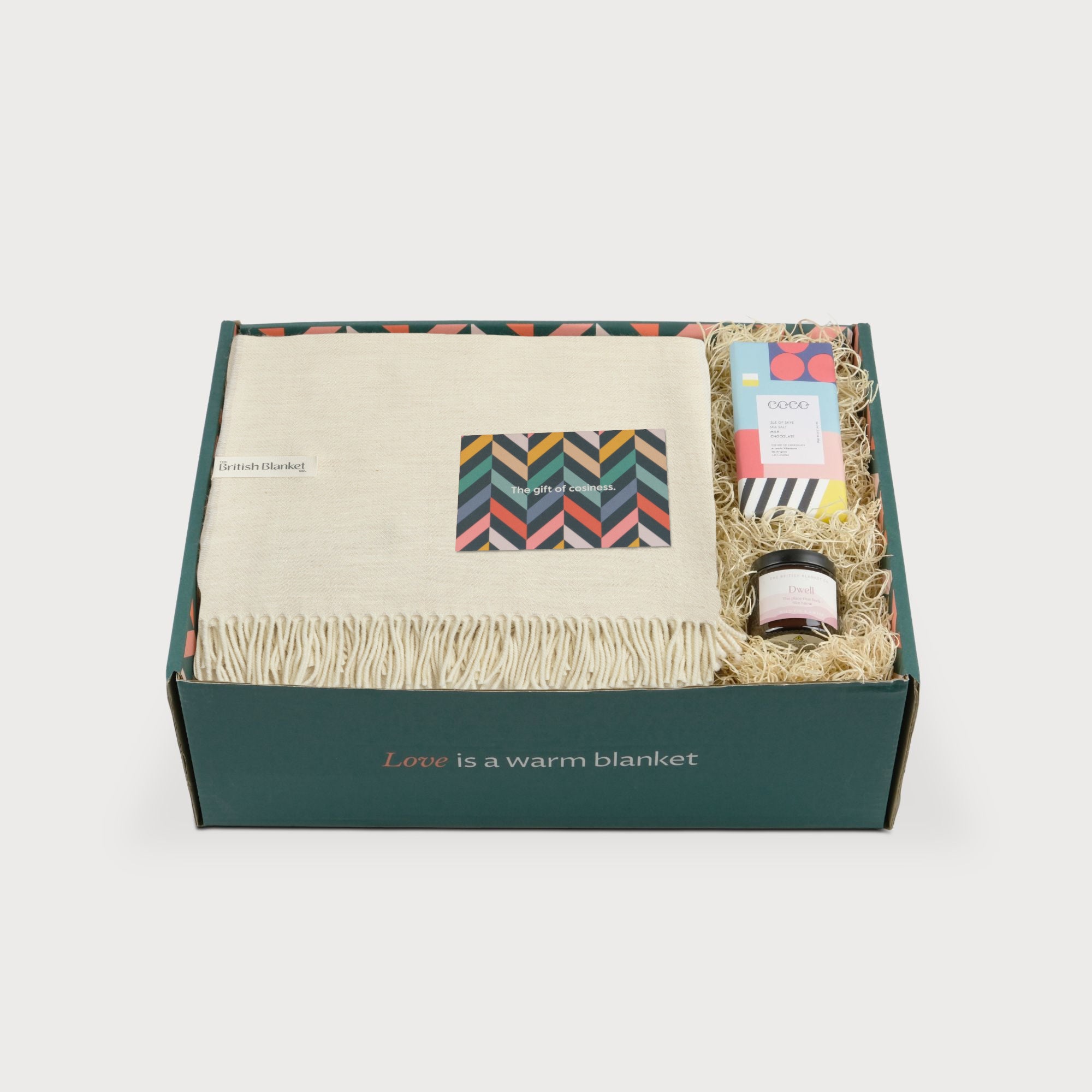 Merino Blanket Gift Box: Cream, featuring a fringed throw, greeting card, sea salt chocolate, and candle, all in a green box labeled “Love is a warm blanket.”