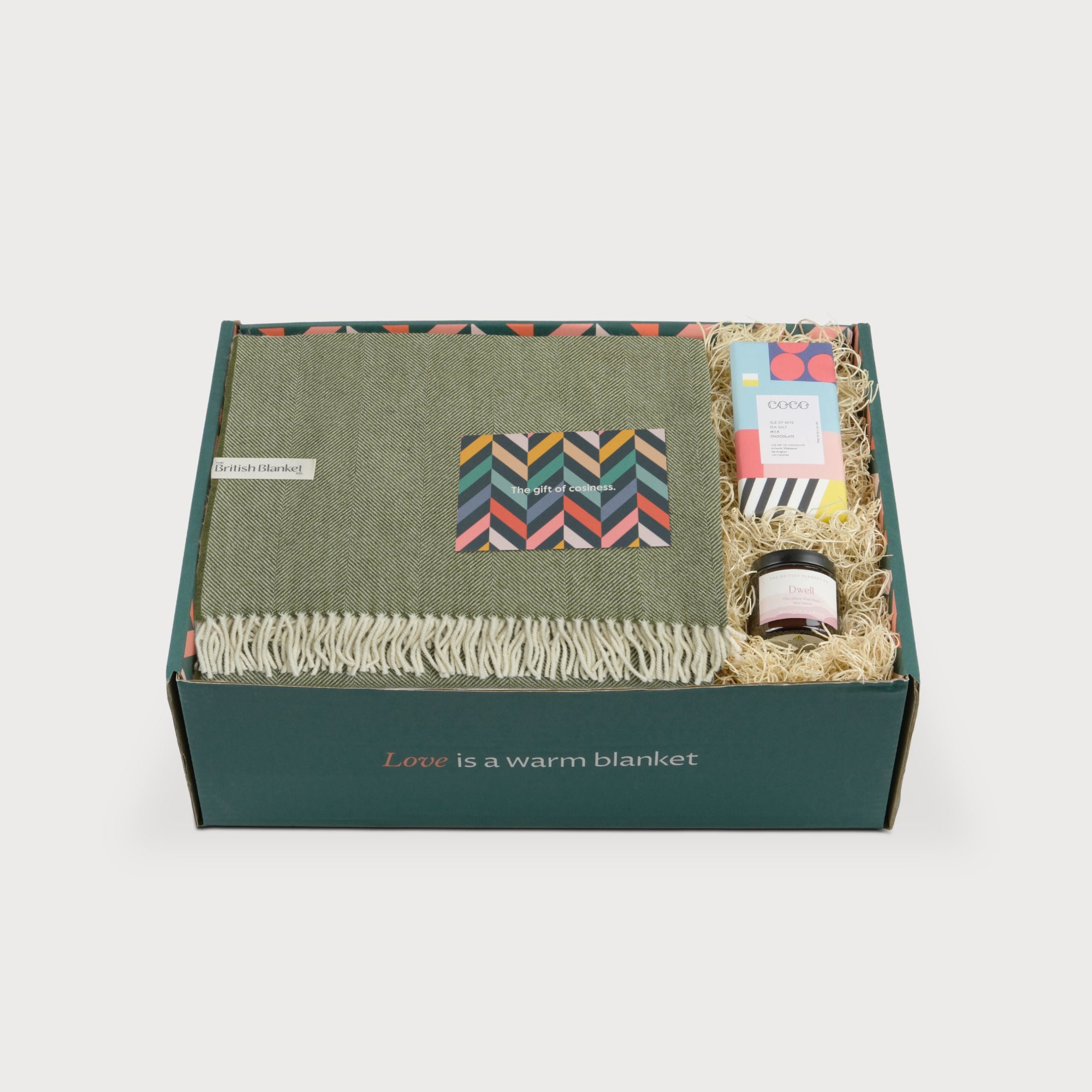 Merino Blanket Gift Box: Olive Green, featuring a wool throw, artisan chocolate, scented candle, and a gift card, all nestled in a teal box.