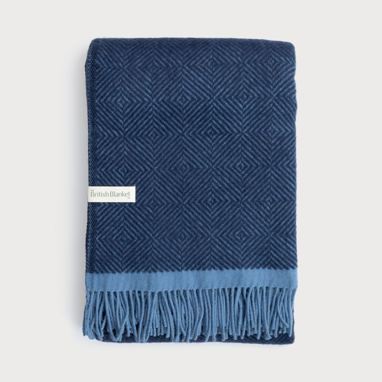 Wildweave Blanket Gift Box: Midnight & Dusk features a navy-blue wool blanket with geometric weave, light-blue fringe, and The British Blanket Co. label.