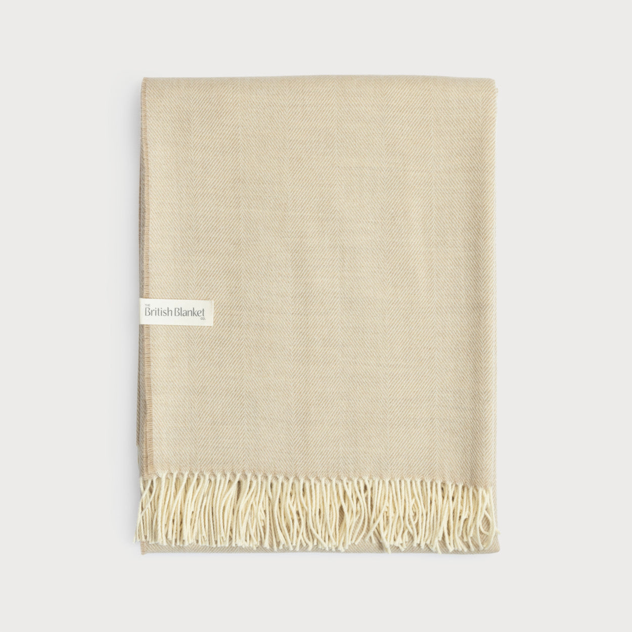 Merino Blanket Gift Box: Basswood featuring a cream-beige wool throw with herringbone weave, fringe, and label. Includes candle, chocolate, message card, and colorful gift box.