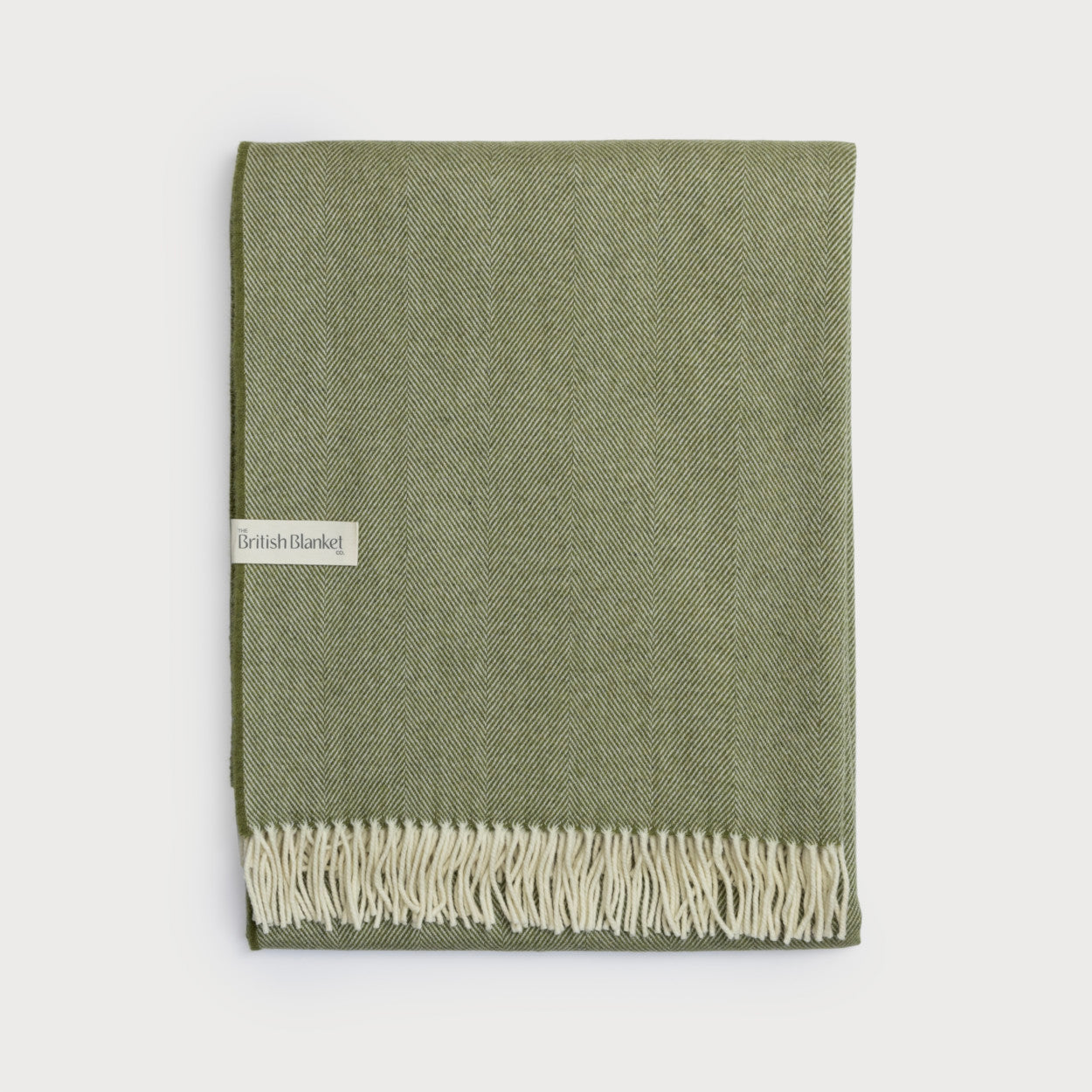 Merino Blanket Gift Box: Olive Green features a folded, olive-green wool blanket with herringbone weave and cream tassels, showcasing The British Blanket Co. label.