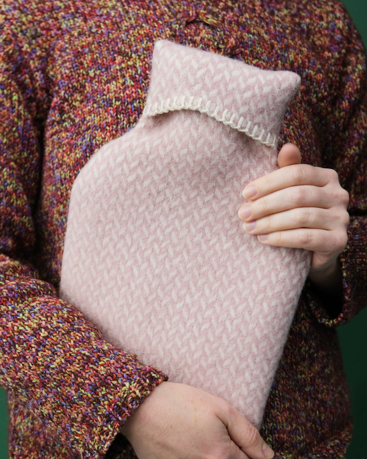 Person holding a wool-covered hot water bottle, showcasing its cosy design and snug fit, ideal for keeping warm on chilly nights.