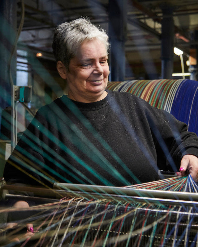 A person operates a loom, weaving the Cosy Crew Reward: 3 For 2 Random Recycled (Small) blanket, showcasing sustainable craftsmanship with upcycled wool threads.