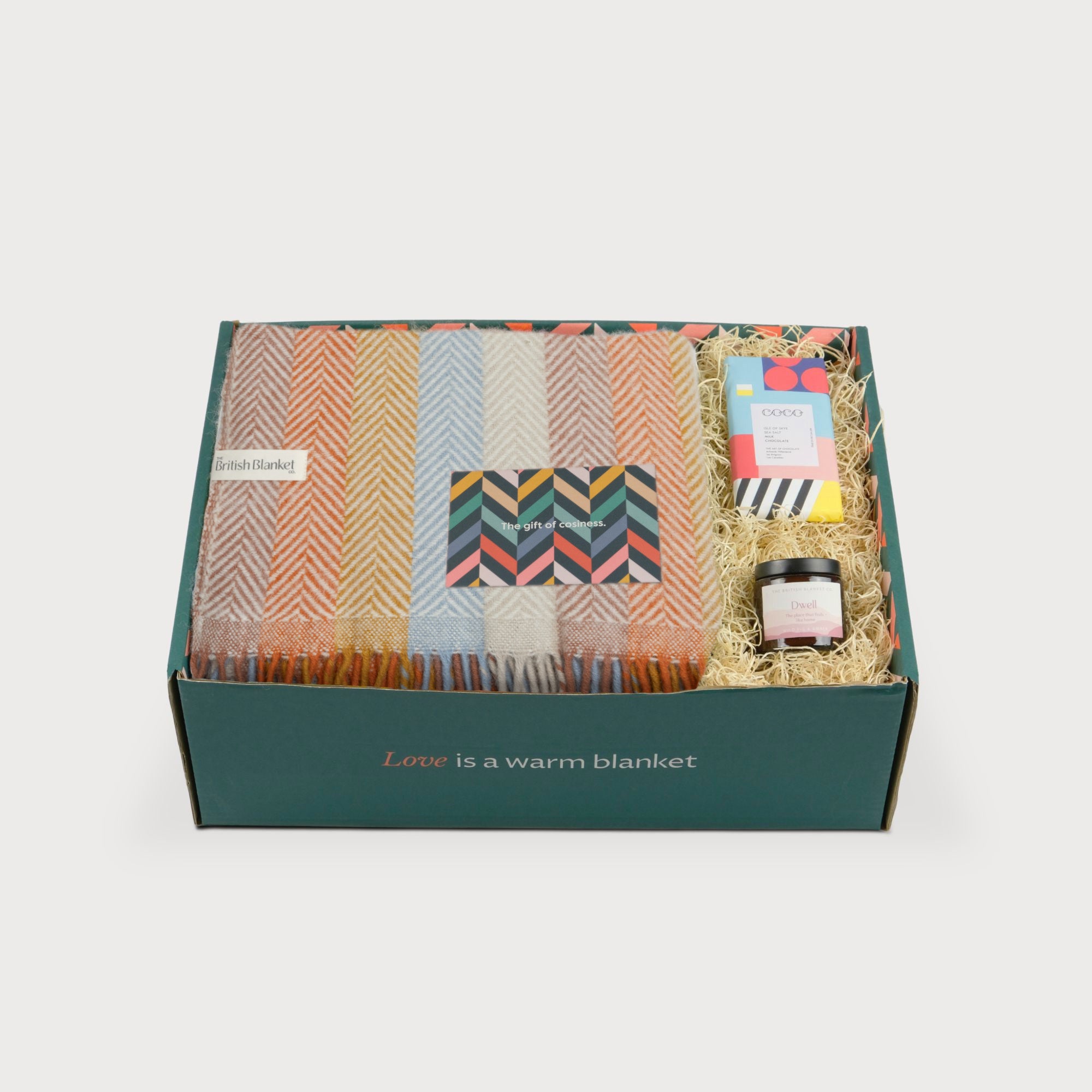 Rainbow Stripe Blanket Gift Box: Boho, includes a herringbone wool blanket, greeting card, COCO chocolate, and Dwell jar, all in a green gift box.