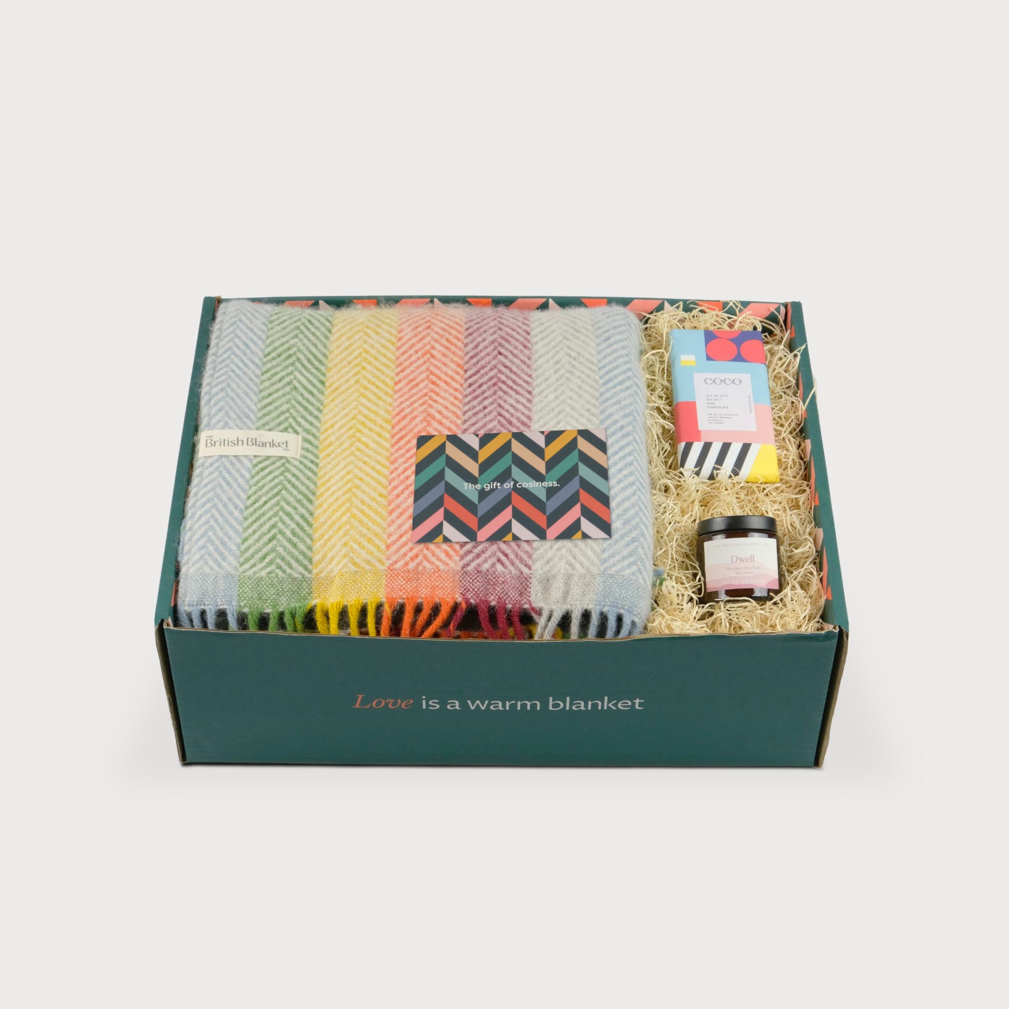 Rainbow Stripe Blanket Gift Box: Bright, includes a folded wool blanket, greeting card, wrapped chocolate, scented jar, and wood-wool, all in a green box.