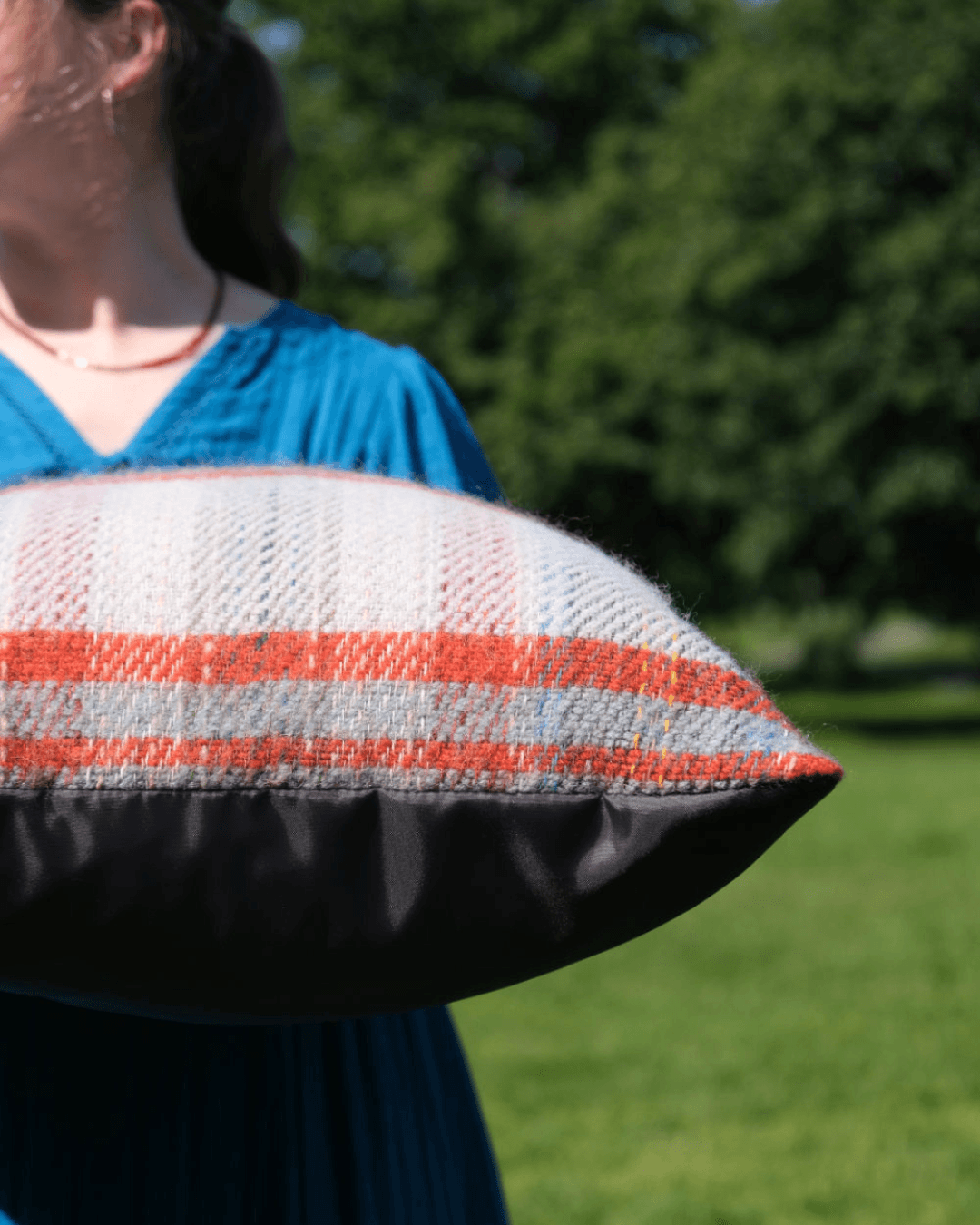Bethan holding Random Recycled Waterproof backed cushion in sunny park