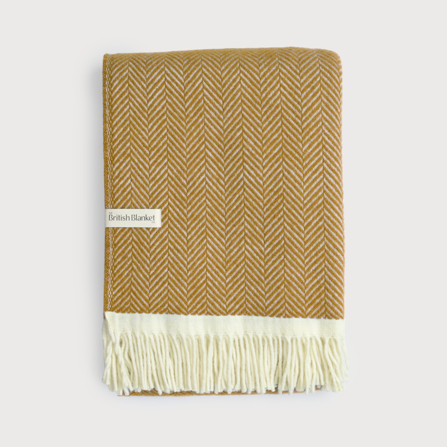 Clifton Blanket Gift Box: Spiced Cider features a mustard-yellow and off-white herringbone wool throw with cream fringe, ideal for gifting alongside chocolate and a scented candle.