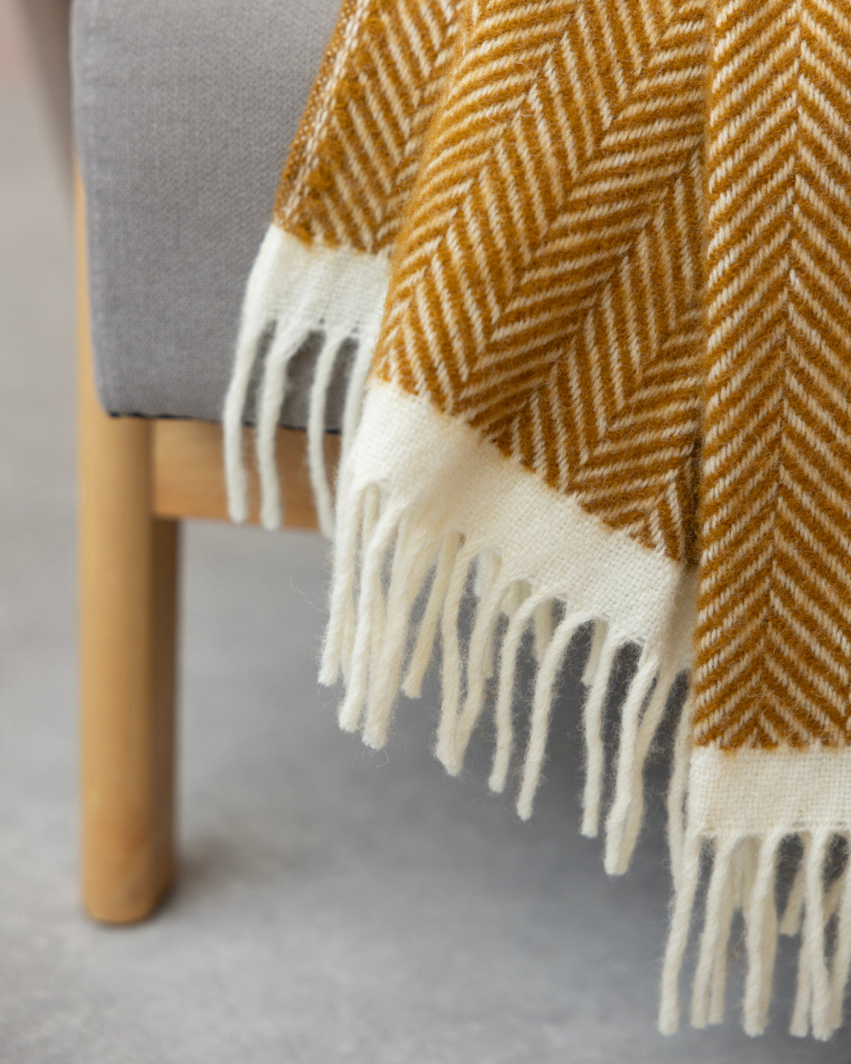 Clifton Blanket Gift Box: Spiced Cider features a gray-upholstered chair with a mustard-yellow herringbone throw, light wood legs, on a smooth light-gray floor.