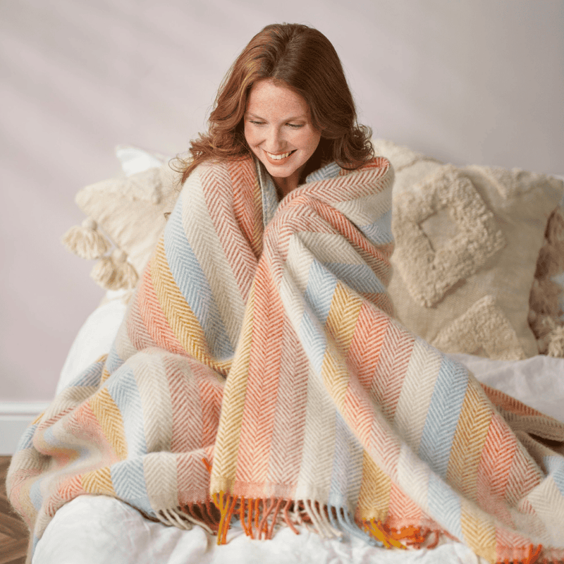 Woman wrapped in a colorful striped rainbow blanket on a bed