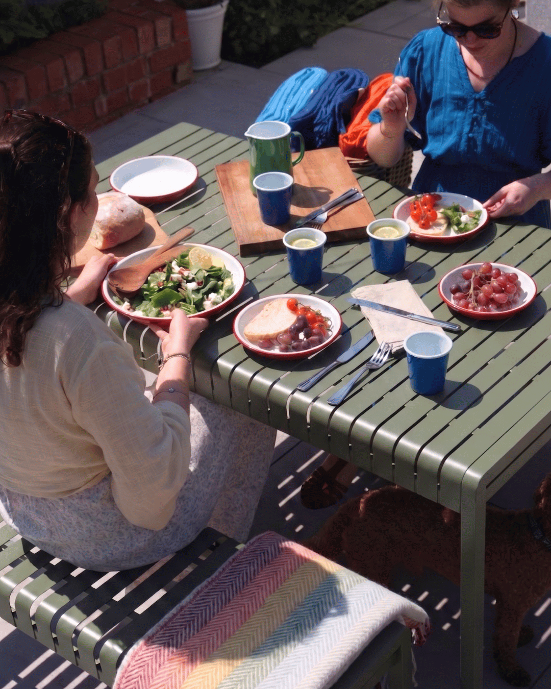 Two people sitting at a green outdoor table with plates of food and drinks.