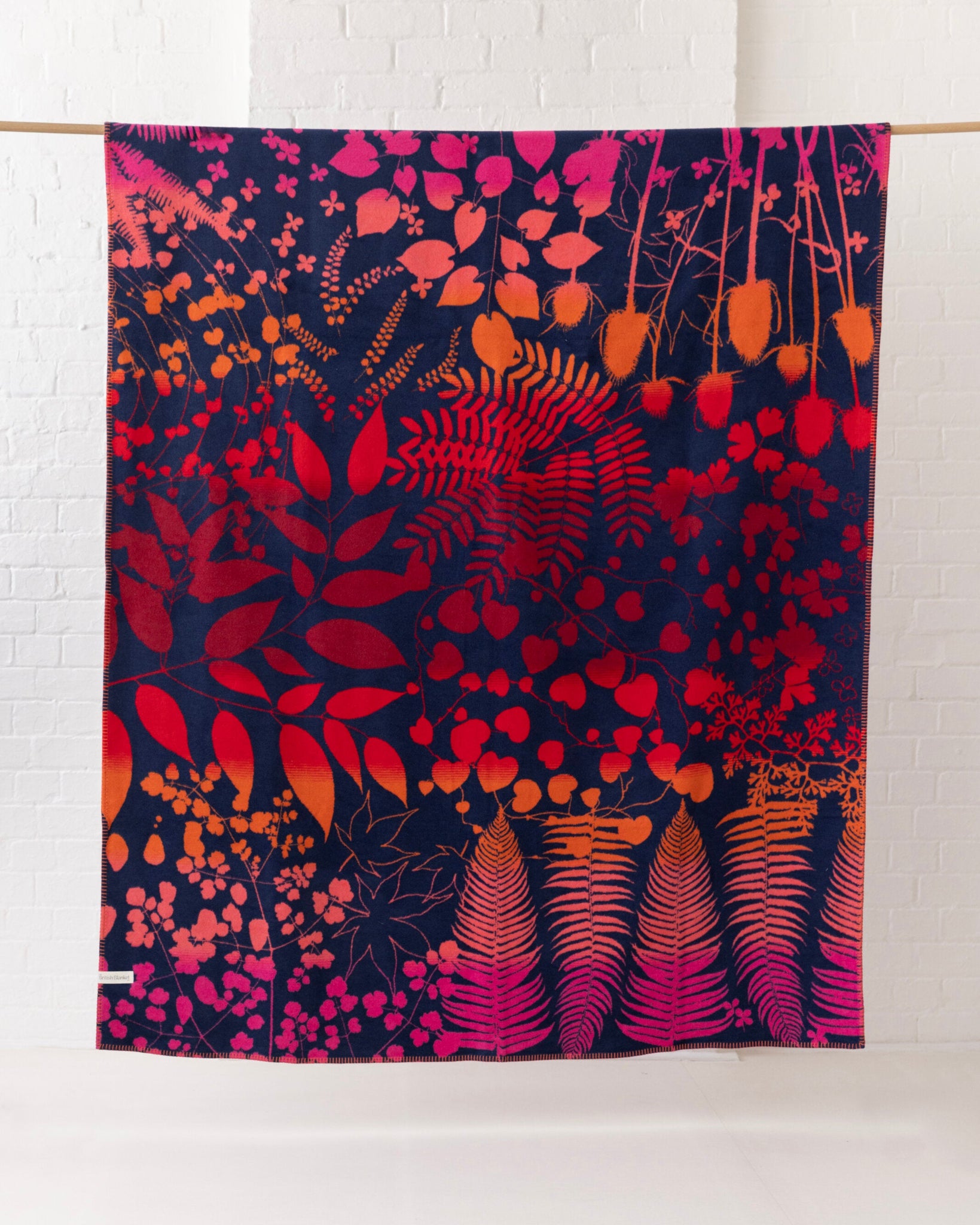Clarissa Hulse Blanket: Indian Summer in Sunset features vibrant botanical silhouettes on a navy base, showcasing fiery ombré hues, enhancing its reversible, recycled cotton design.
