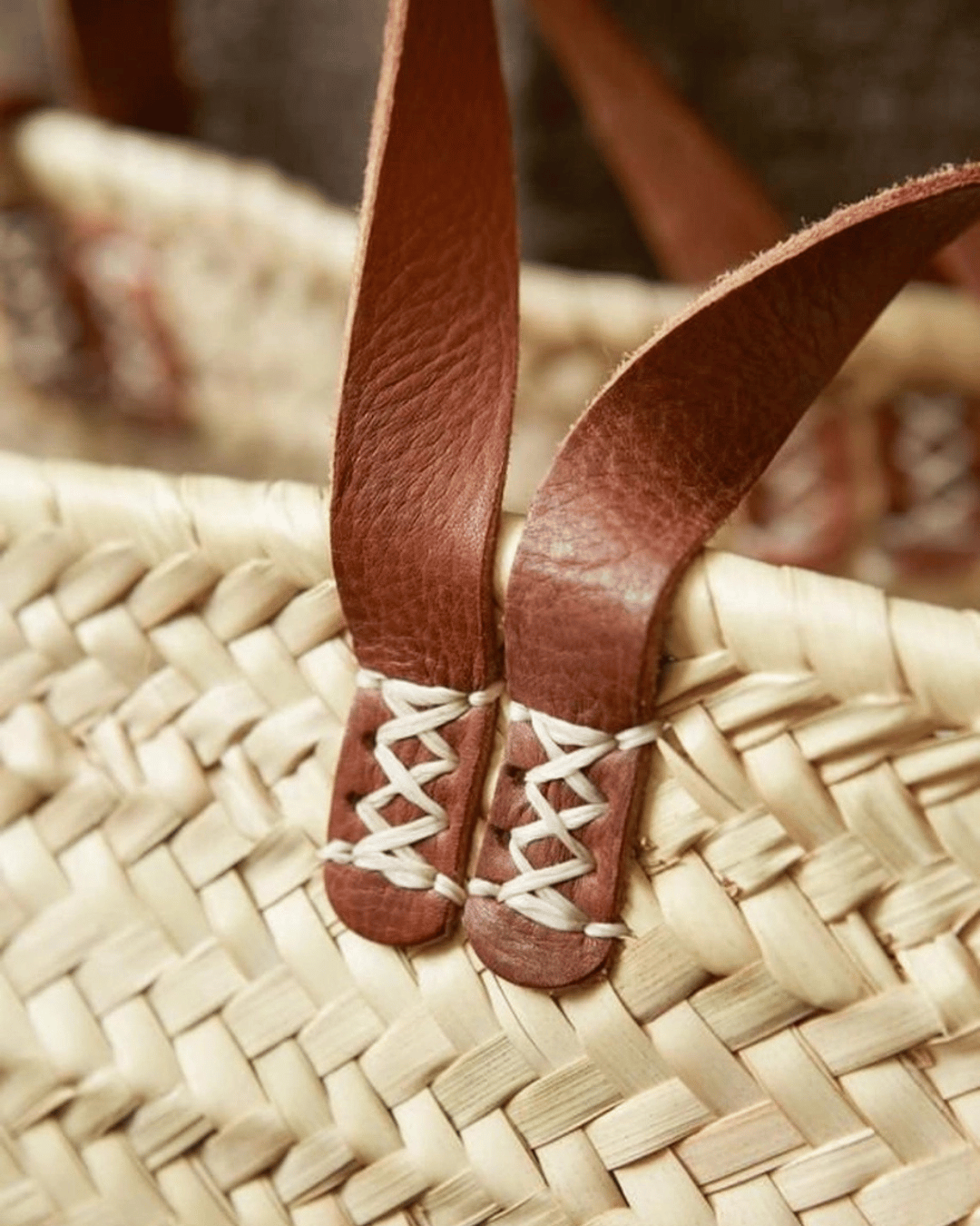 Close-up of a woven straw tote bag with brown leather straps.