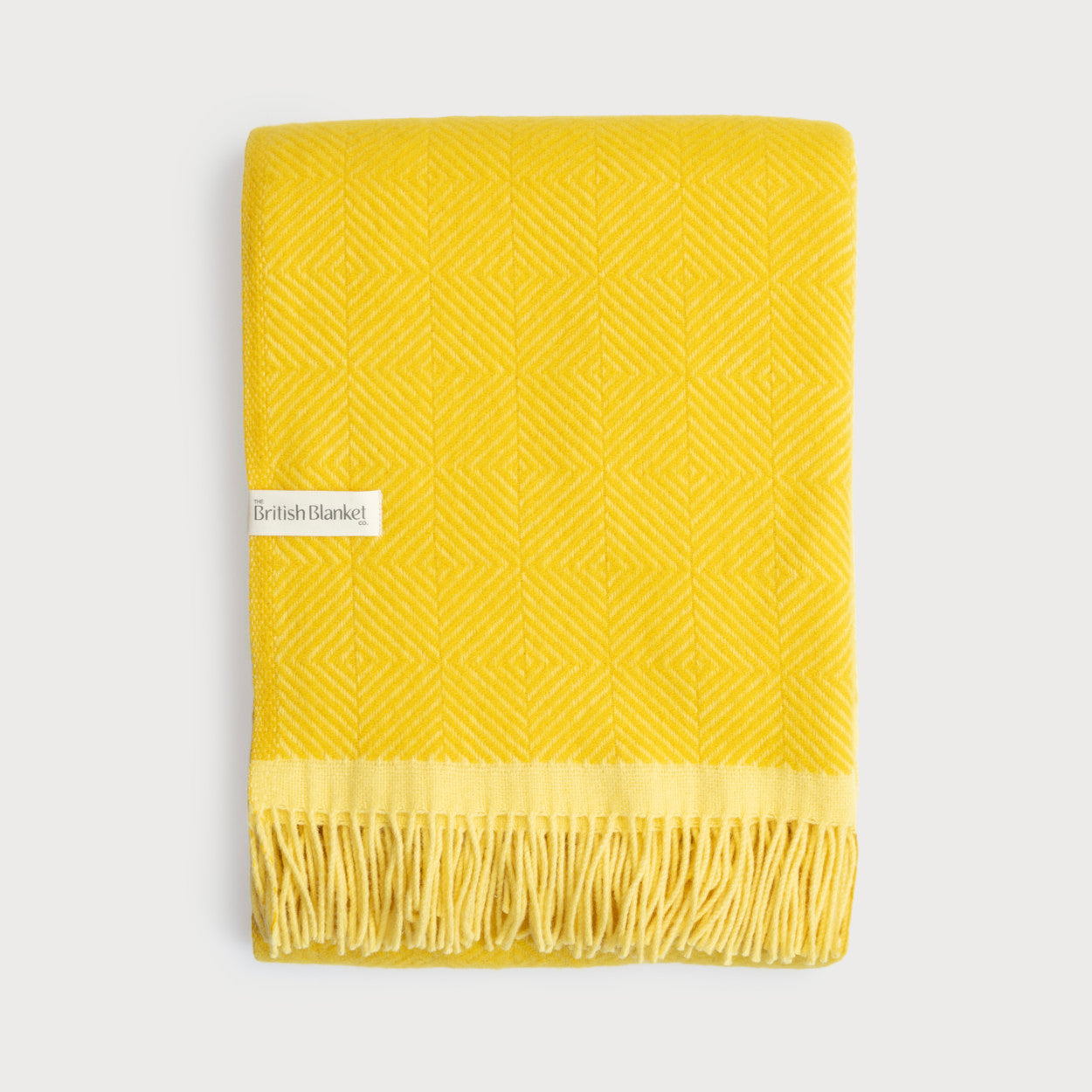 Wildweave Blanket Gift Box: Buttercup & Primrose features a folded yellow wool blanket with a diamond pattern, tassel fringe, and a The British Blanket Co. label.