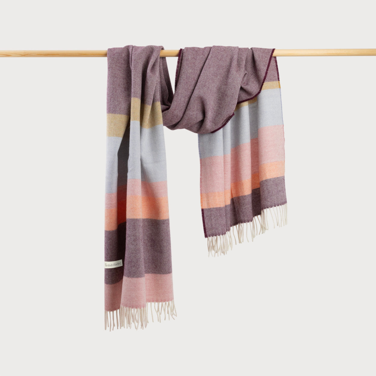 Oversized Blanket Scarf: Berry Stripe, shown draped on a bar, features a luxurious merino lambswool texture with fringe detailing, ideal for warmth and style.