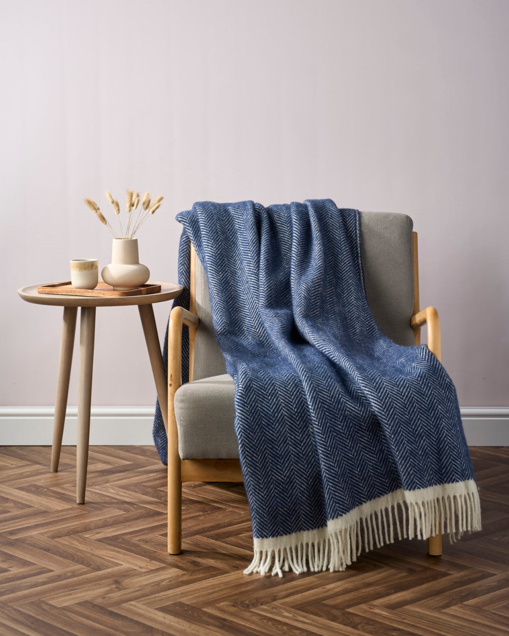 Clifton Blanket Hamper: Brunel in a cozy corner with a light-gray armchair, blue throw, wooden side table, and neutral-tone vase with dried grasses.