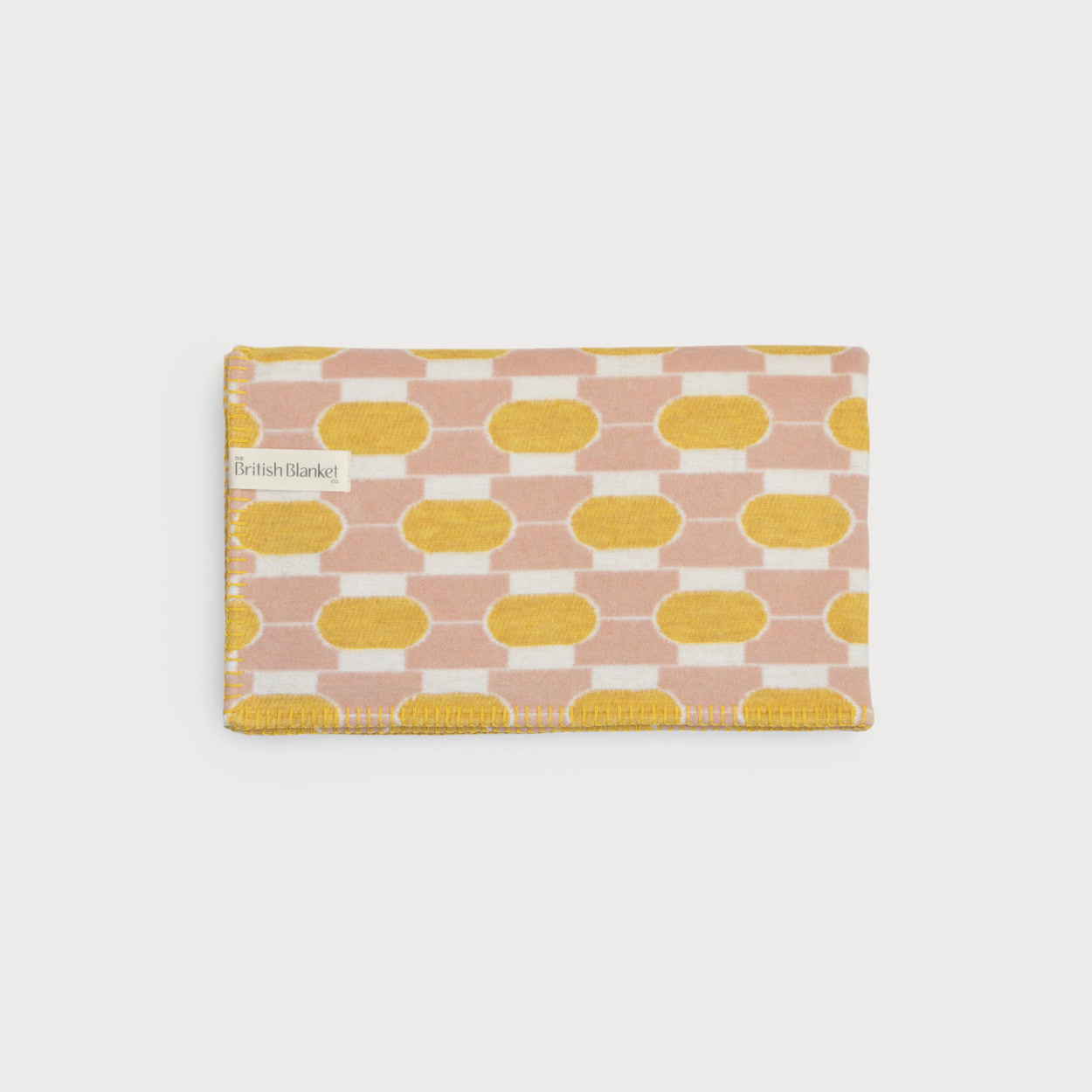 The Cloud Cotton Baby Blanket Gift Box: Boatyard Glow features a folded wool blanket with a geometric pattern, showcasing mustard-yellow ovals on a soft peach background.
