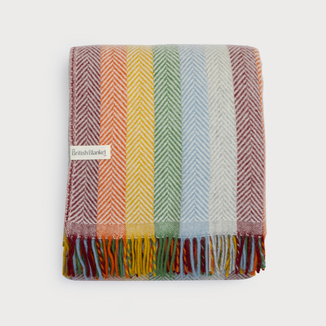 Rainbow Stripe Blanket Gift Box: Bright features a folded woollen throw with herringbone weave, rainbow stripes, fringed edge, and a The British Blanket Co. label.