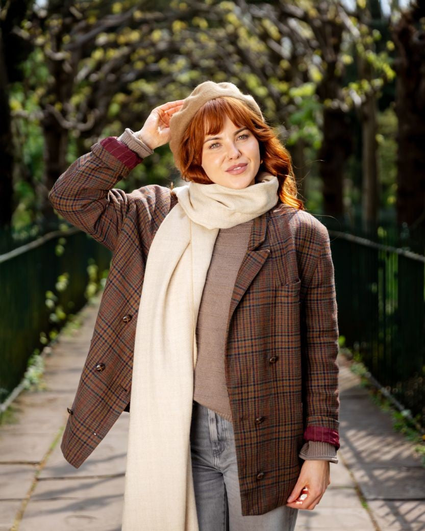 Woman wearing Wool Beret Hat: Camel Brown, adjusting it with a smile; the beret highlights a structured, breathable design amidst a serene tree-lined pathway.