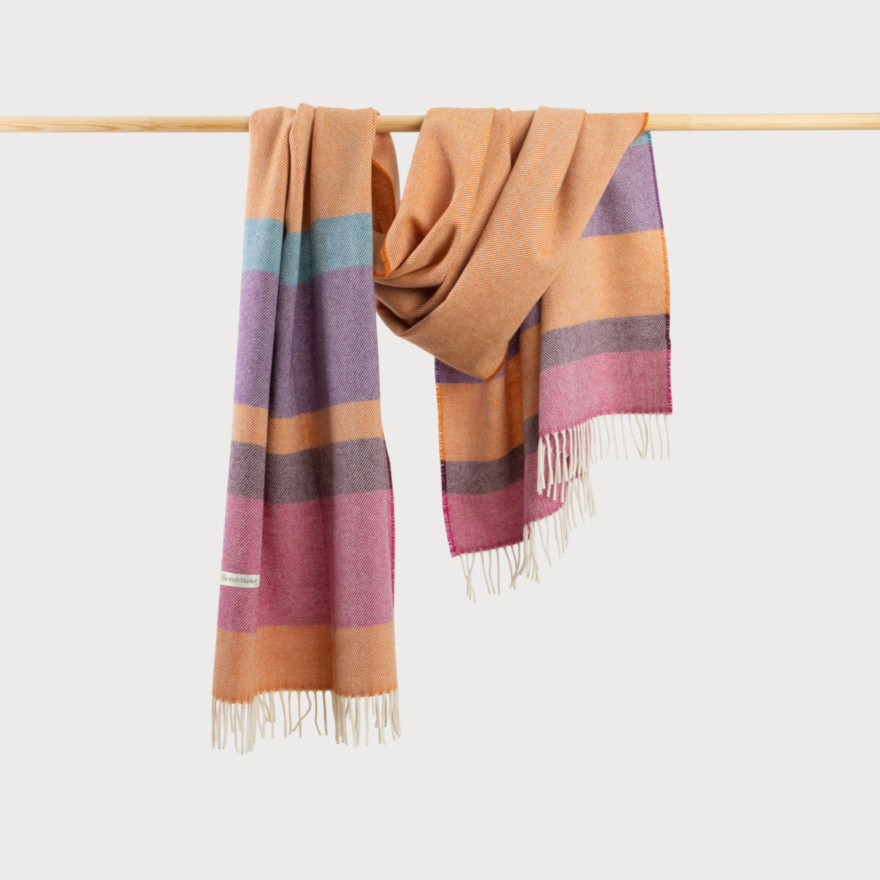 Oversized Blanket Scarf: Dahlia Stripe, featuring a fine herringbone weave and fringe, draped on a bar.