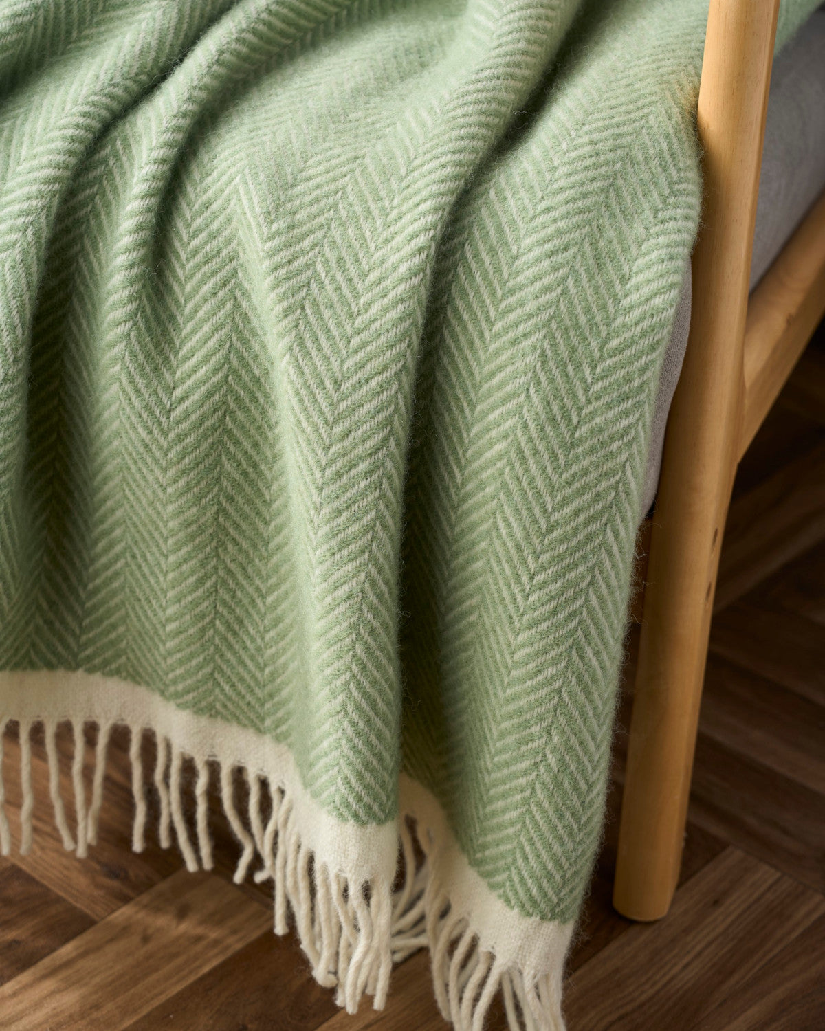 Clifton Blanket Hamper: Birdcage shown draped over light-wood furniture, featuring a woven texture and cream fringe, enhancing a cozy and elegant setting.