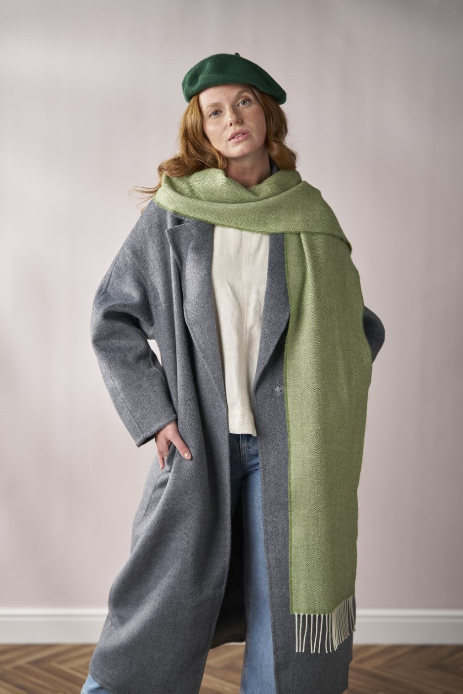 Woman in gray overcoat models Scarf Gift Box: Apple Herringbone, featuring a moss-green scarf, ideal for adding warmth and color to outfits.