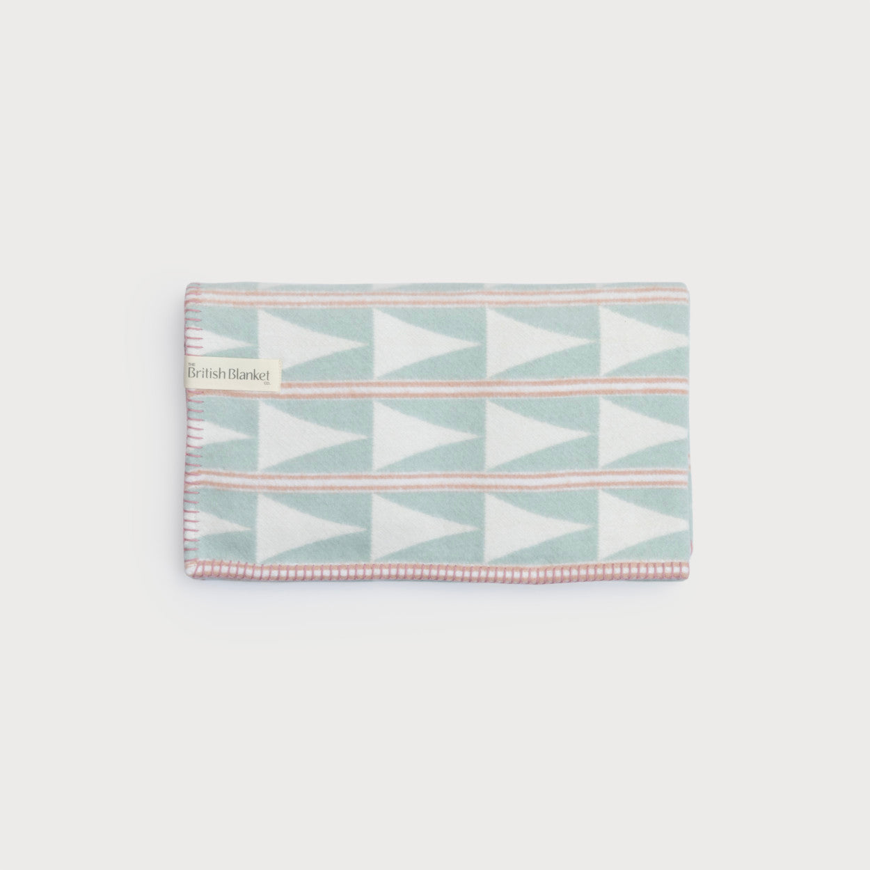 Baby Blanket Hamper: Cloud Cotton featuring a folded wool throw with geometric white triangles, peach stripes, and a British Blanket label, part of a new baby gift set.