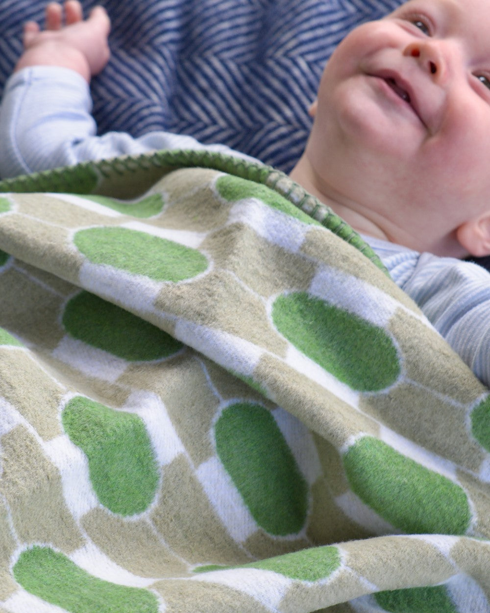 Cloud Cotton Baby Blanket: Boatyard Botanic, featuring a baby lying on a green geometric-patterned blanket, showcasing its softness and comfort.
