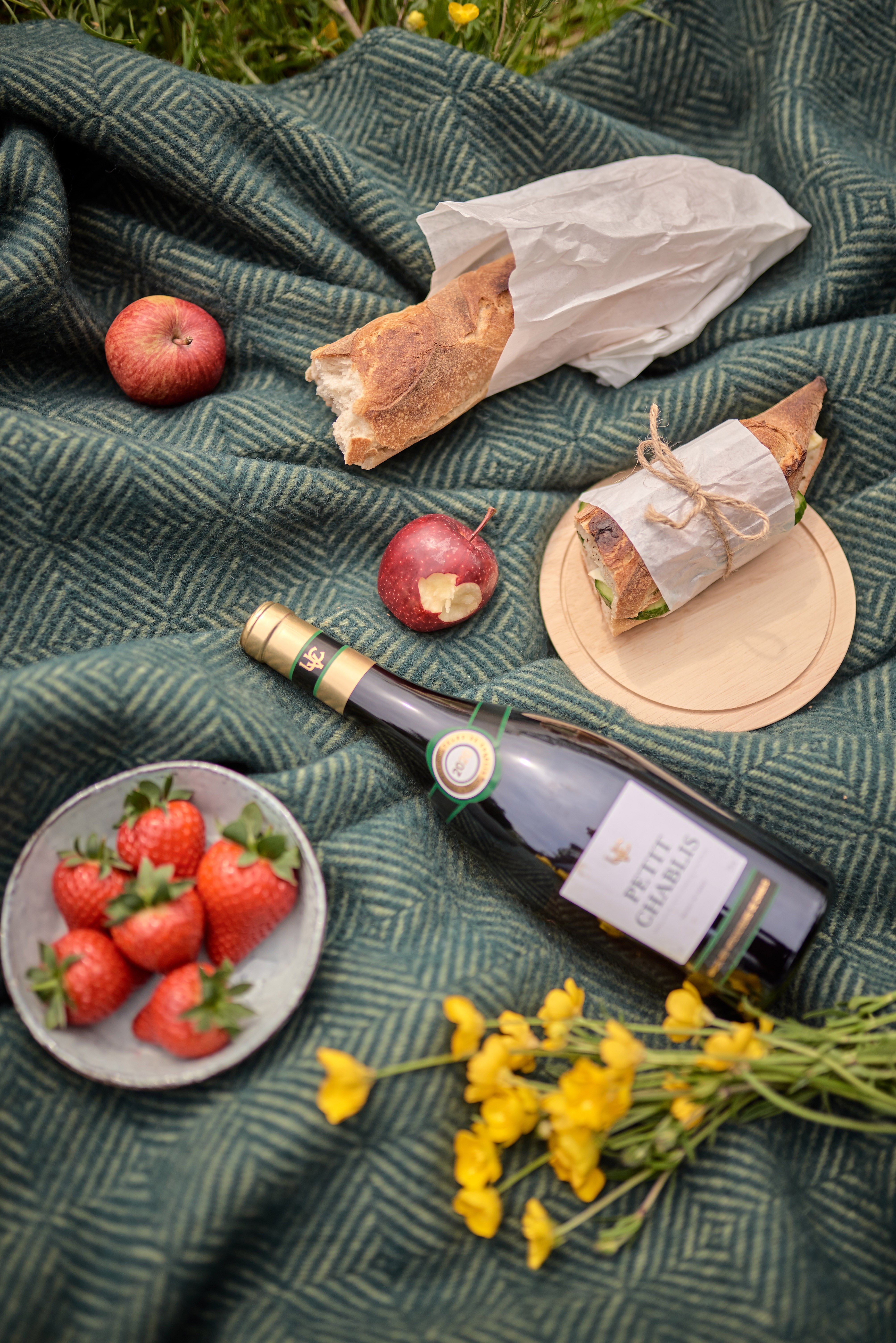 Waterproof Picnic Blanket: Juniper and Moss, displayed with a bottle of wine, a sandwich, strawberries, and other picnic foods on it.