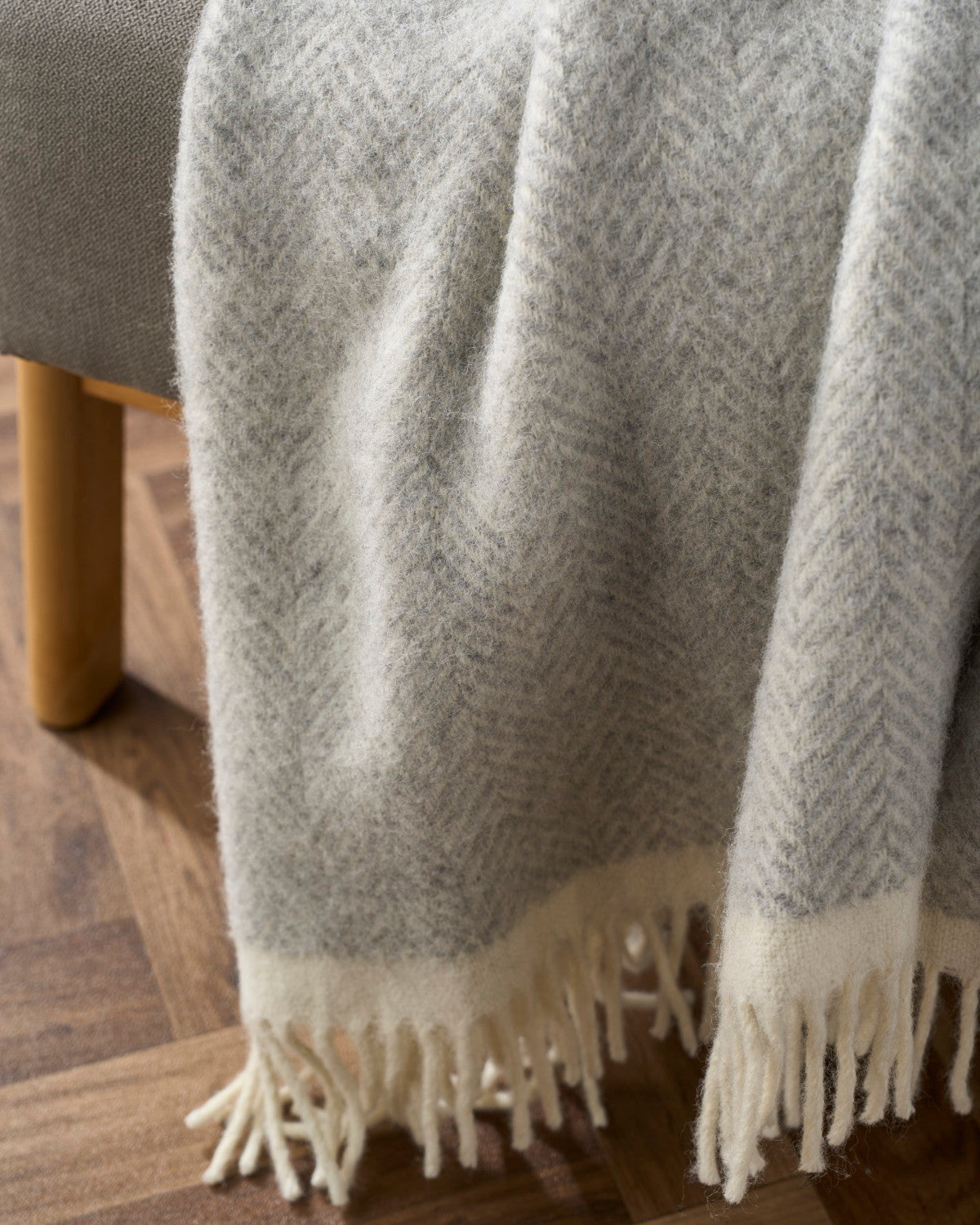 Clifton Blanket Hamper: Blanquette, a soft wool throw with a herringbone pattern and fringed edges, draped over a piece of upholstered furniture.