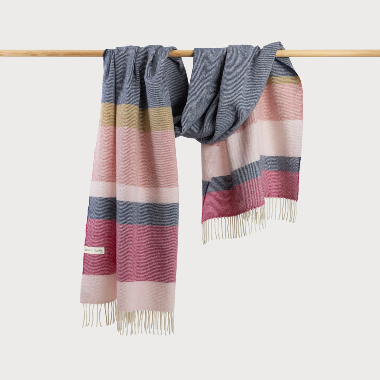 Oversized Blanket Scarf: Indigo Stripe, woven from plush merino lambswool, hanging on a wooden bar with a striped pattern.