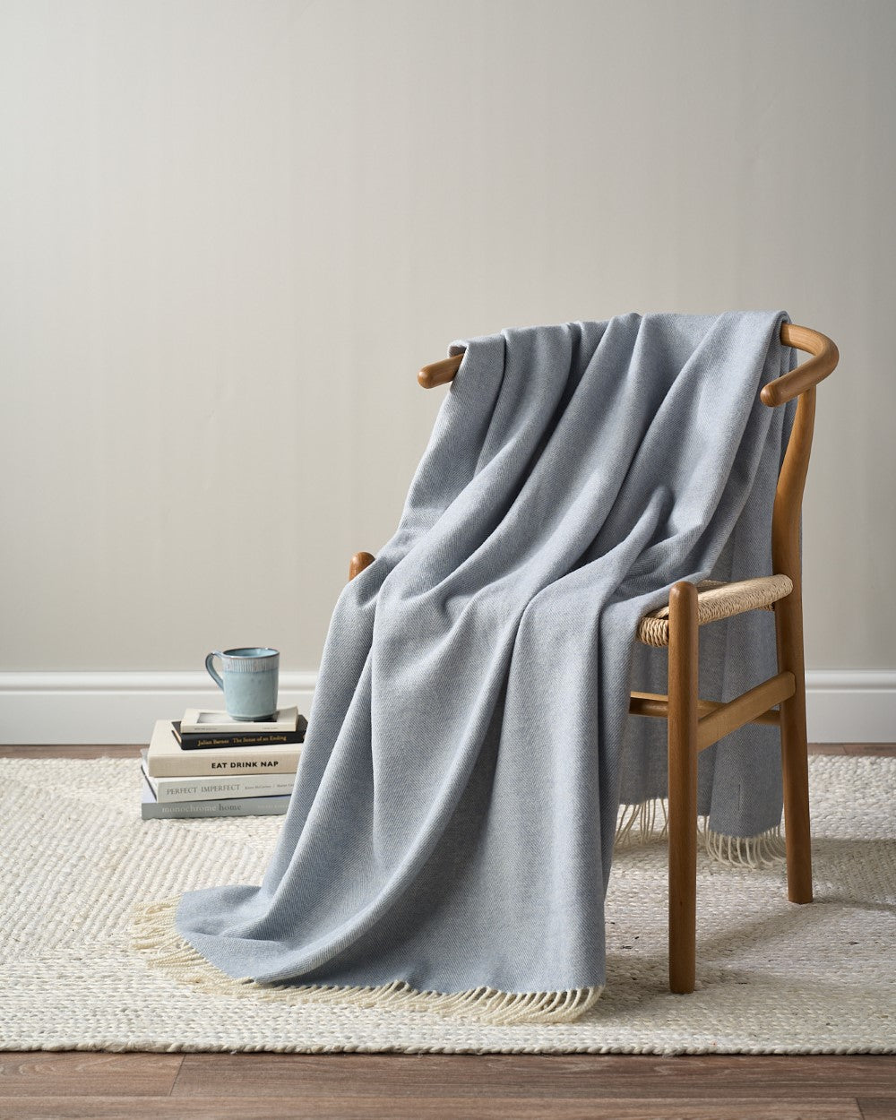 Merino Blanket Gift Box: Smoke Blue, featuring a wool blanket, throw, books, and a mug on a cozy chair setup, perfect for gifting.