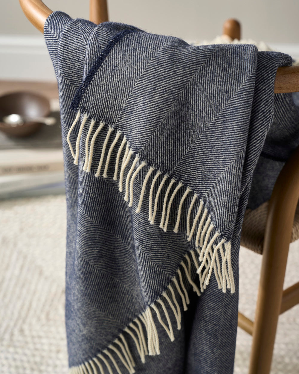 Merino Blanket Gift Box: Navy Blue, featuring a blue-and-white herringbone pattern blanket with cream fringe, draped over a wooden chair.