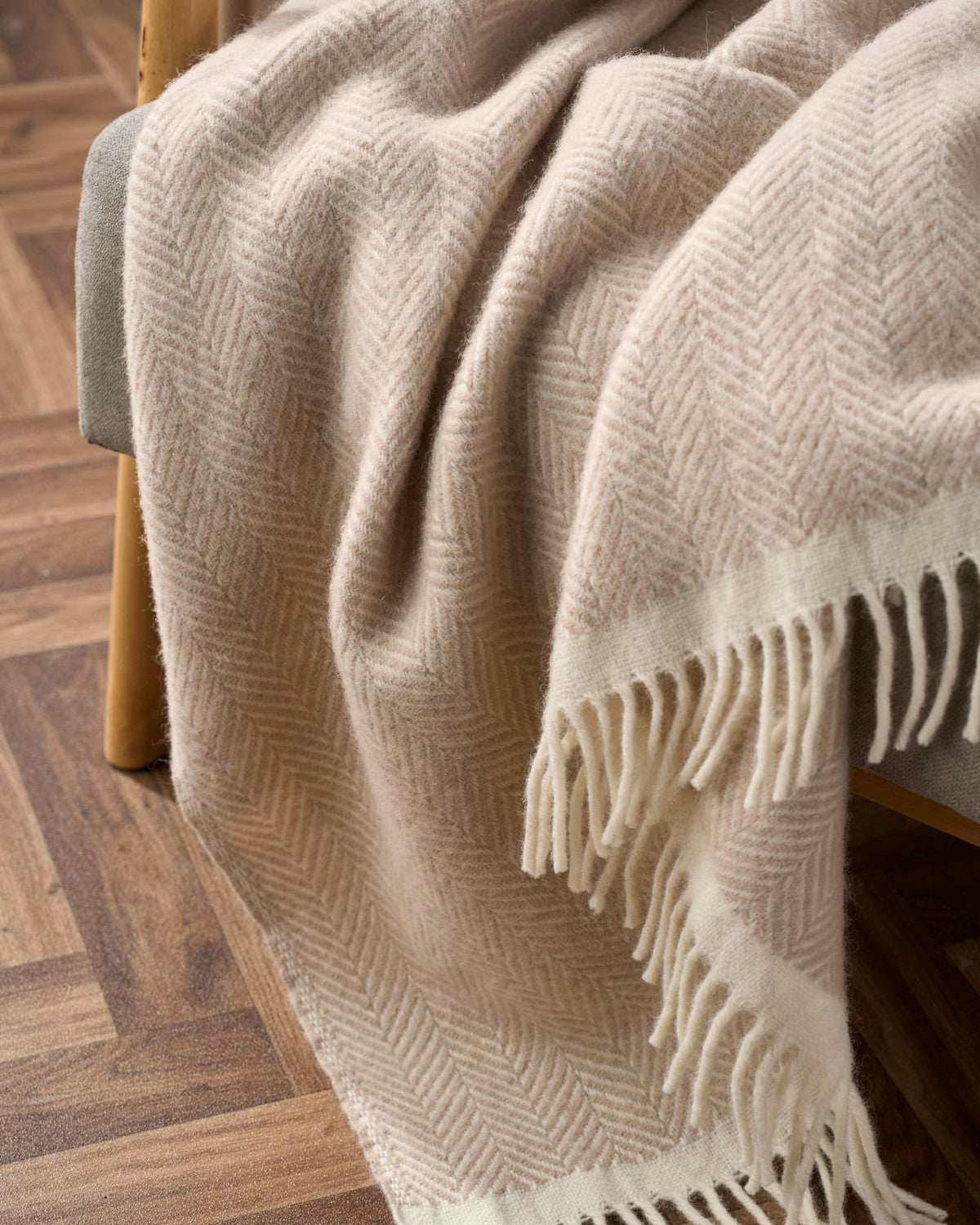 The Christmas Blanket Gift Box: Bath Stone features a woven throw with a subtle herringbone pattern and fringed ends, elegantly draped over a padded bench.