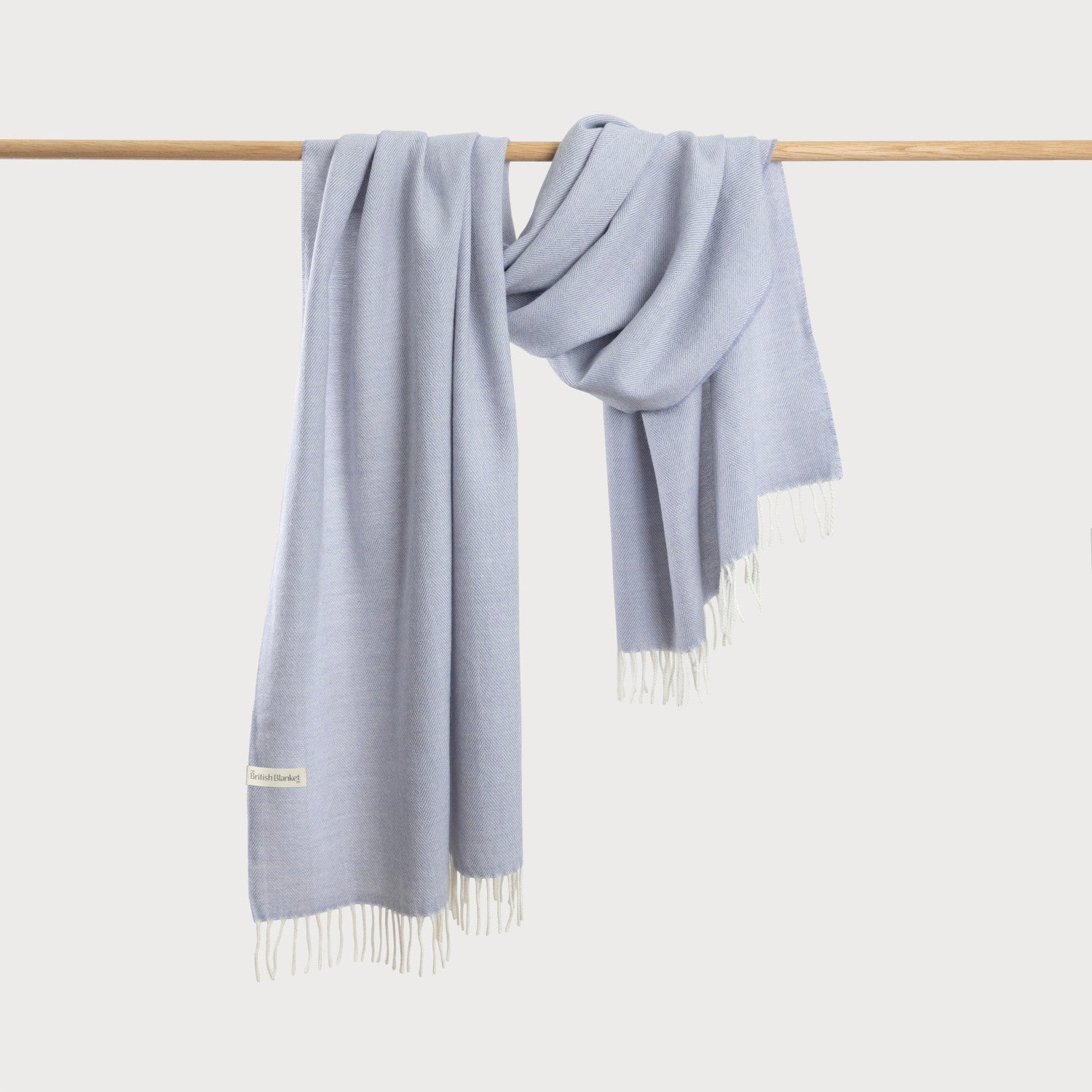 Oversized Blanket Scarf: Smoke, draped over a wooden rod, featuring a small “British Blanket” label and white fringe at the ends.