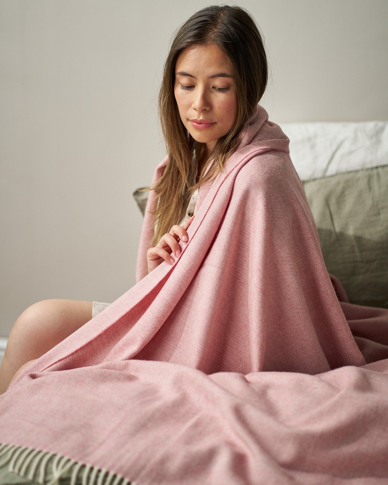 Young woman embraces Merino Blanket Gift Box: Blush Pink, showcasing its herringbone weave and fringed edges, embodying warmth and elegance.