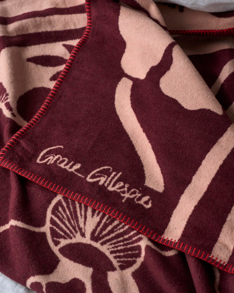Decorative cotton blanket with a bold floral design in shades of pink and burgundy, featuring the Grace Gillespie brand name.