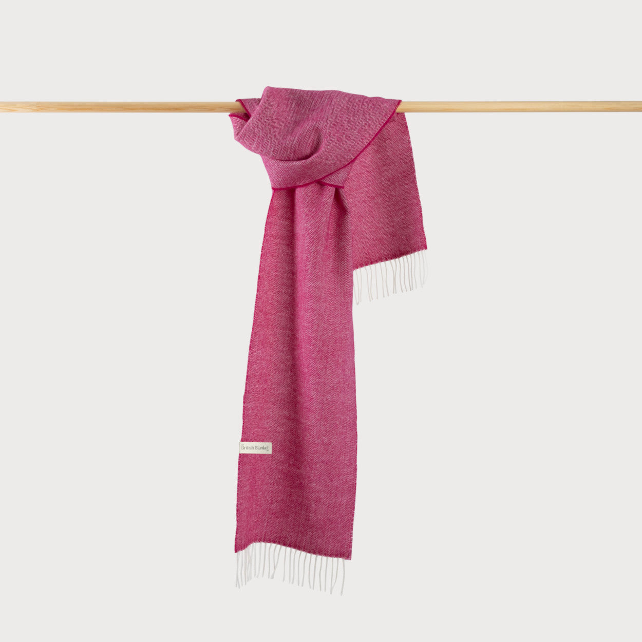 Herringbone Scarf: Magenta draped on a wooden bar, showcasing its fringed edges and fine pattern, highlighting its luxurious softness.