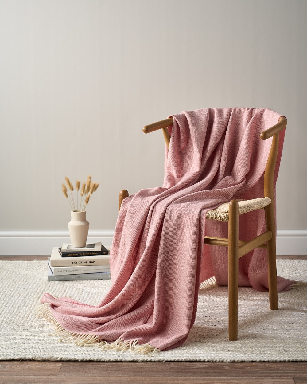 Merino Blanket Gift Box: Blush Pink showcased on a chair with a woven seat, featuring a draped throw blanket, perfect for gifting on special occasions.