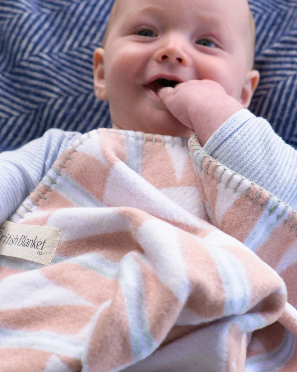 Baby wrapped in a Cloud Cotton Baby Blanket Gift Box: Harmony Blossom, a soft pastel pink and white blanket, looking calm on a patterned surface.