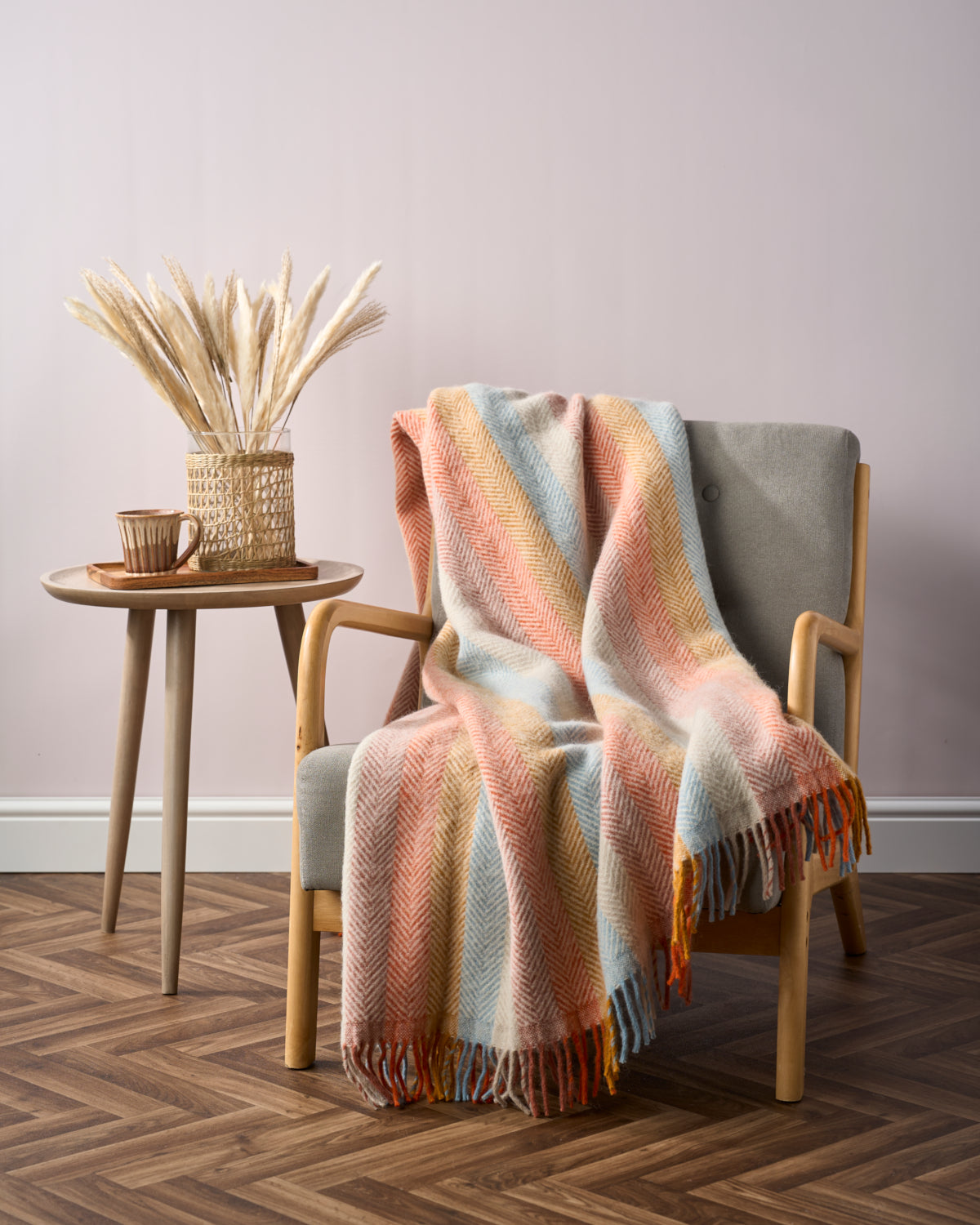 Rainbow Stripe Blanket Gift Box: Boho, featuring a pastel-striped throw on a light-wood armchair, accompanied by a candle and sea salt chocolate on a side table.