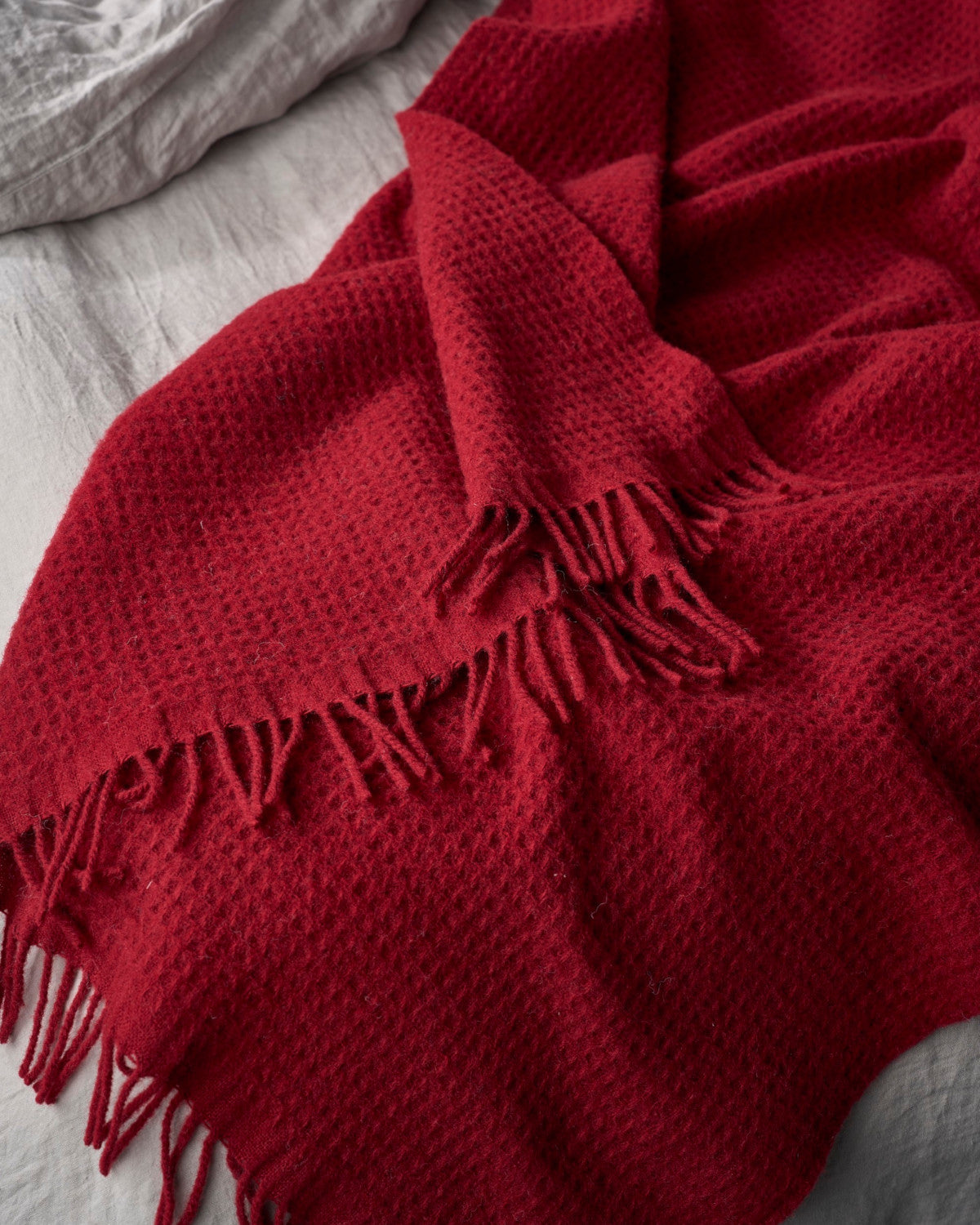 The Bright Friday Blanket Bundle: Air Balloon features a waffle-textured throw with fringed ends, elegantly draped over a bedspread, showcasing its cozy, inviting design.