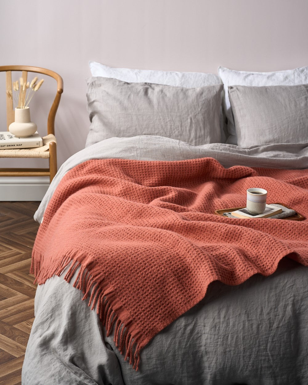 Bedroom with Bright Friday Blanket Bundle: Brunswick, featuring a waffle-knit throw with fringe on a bed, complemented by a wooden tray, mug, and books.