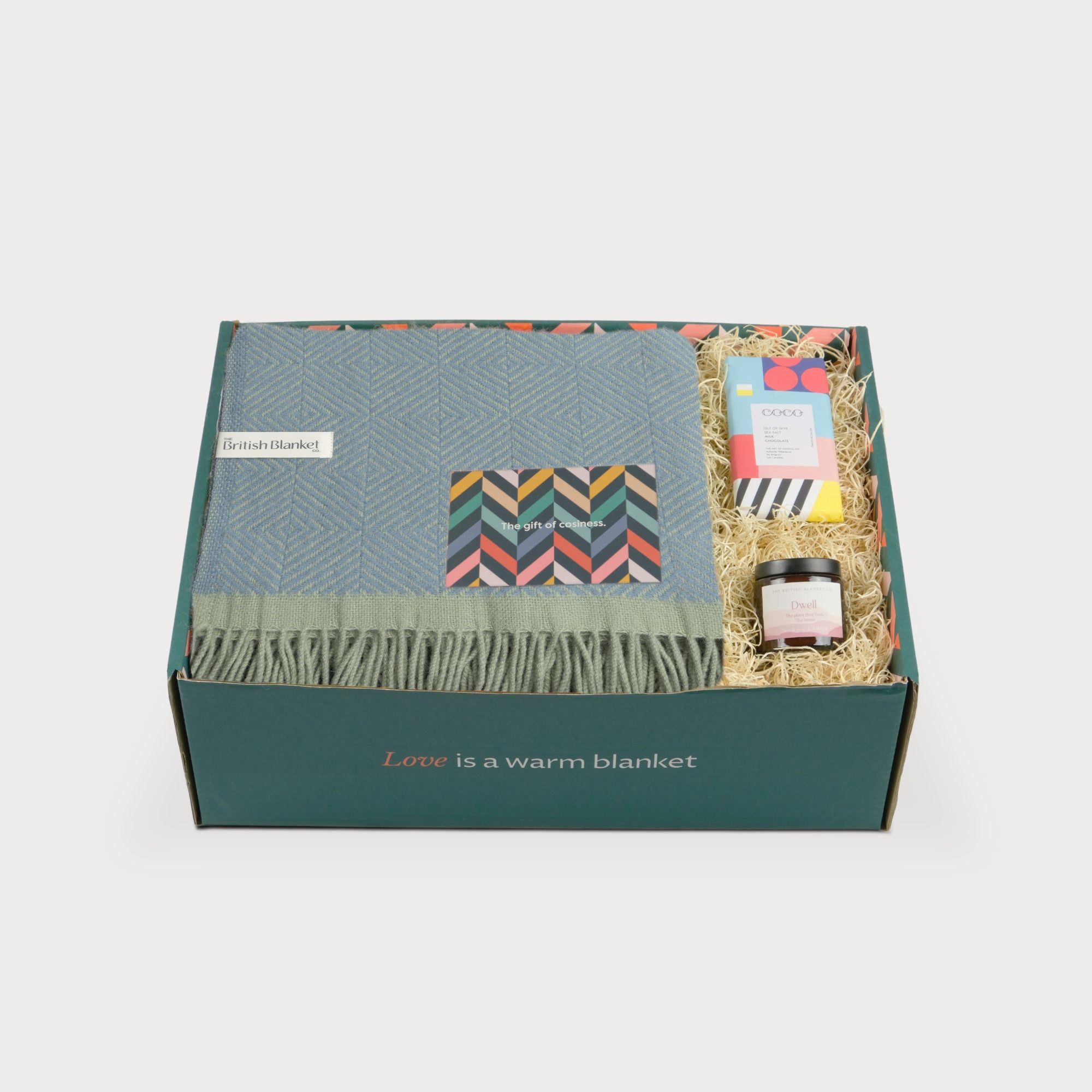 Wildweave Blanket Gift Box: Sea Holly & Lichen features a blue-green wool blanket, sea salt chocolate, amber candle, and greeting card in a cozy gift box.