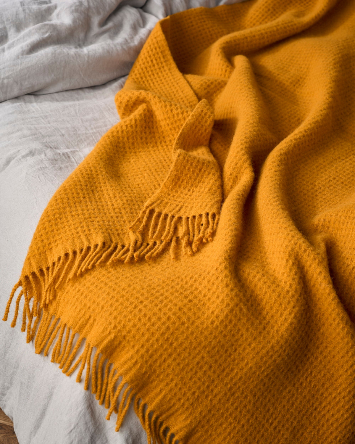 Bright Friday Blanket Bundle: Ashton, featuring a soft waffle-weave throw with fringe, draped over light gray bedding, showcasing a cozy and stylish addition to any room.