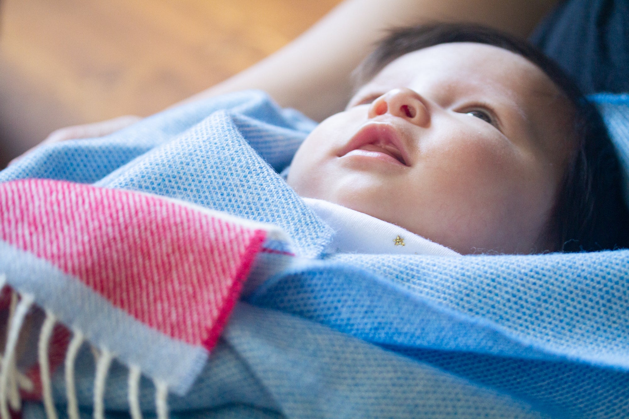 A baby wrapped up with a red and blue lambswool baby blanket