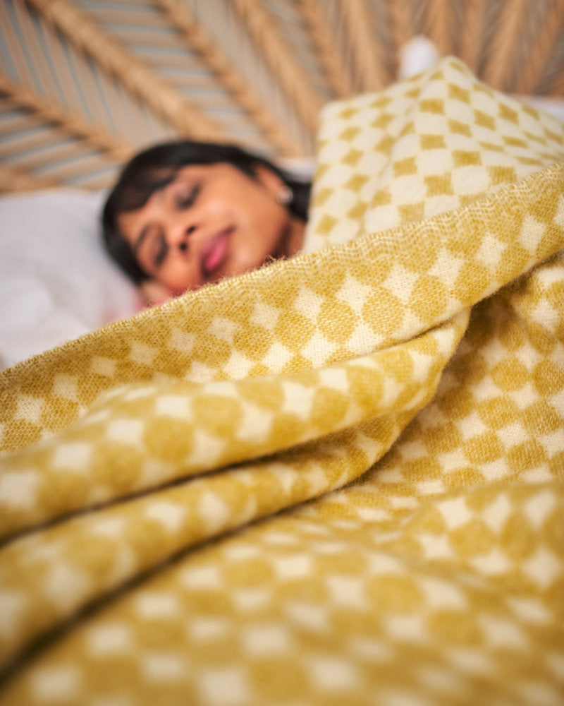 woman sleeping in bed with yellow blanket throw from The British Blanket Company
